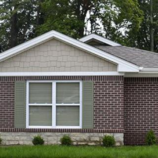 A suburban brick house with green shutters and neatly trimmed lawn.