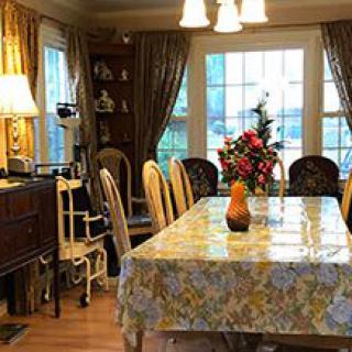 A cozy dining room with a floral tablecloth, chairs, and a centerpiece of flowers.