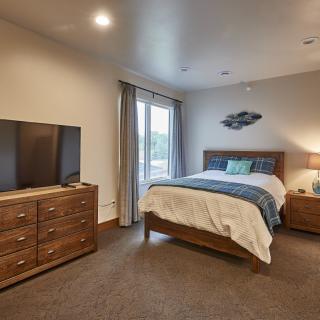 A cozy bedroom with a neatly made bed, wooden dresser, and a flat-screen TV.