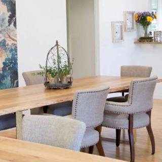 A modern dining room with a wooden table, upholstered chairs, and decorative elements including a plant centerpiece and wall art.