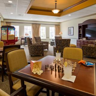 A cozy living room with a chess board on the table, surrounded by comfortable seating and a popcorn machine in the corner.