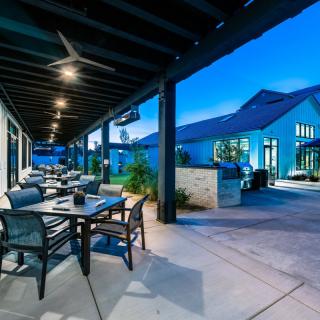 A modern outdoor restaurant patio in the evening with tables, chairs, and ambient lighting.