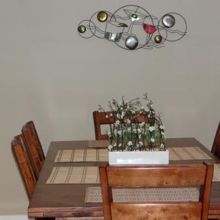 A cozy dining area with a wooden table and chairs, adorned with a modern wall art piece and a centerpiece of potted plants.