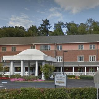 A hotel building with a prominent entrance featuring white columns and a landscaped parking area.