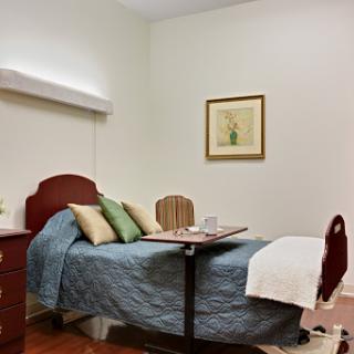 A cozy hospital room featuring a bed with pillows, a table, and decorative wall art.