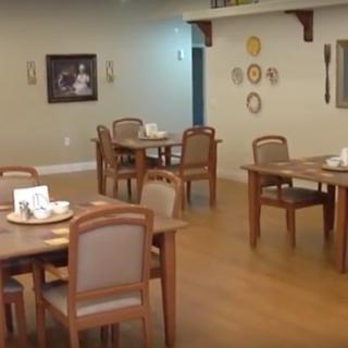An empty dining room with tables and chairs, decorated with wall art and a wooden floor.