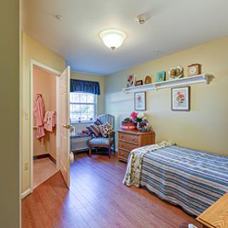 A cozy bedroom with a single bed, wooden flooring, and decorated shelves.