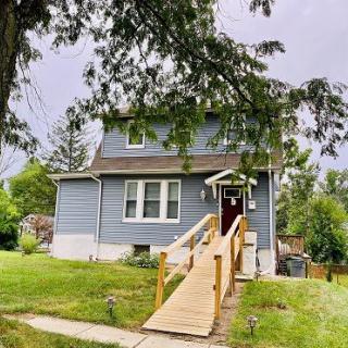 A charming two-story house with a wooden accessibility ramp and a well-maintained front yard.