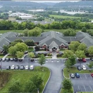 An aerial view of a large building complex surrounded by trees, with a parking lot in the foreground.