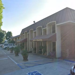 A view of a building with an adjacent parking lot and trees under sunlight.