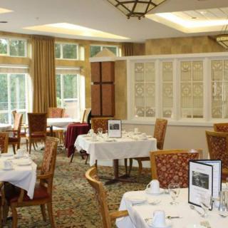 A cozy restaurant dining area with elegantly set tables and wooden chairs, featuring large windows and warm ambient lighting.