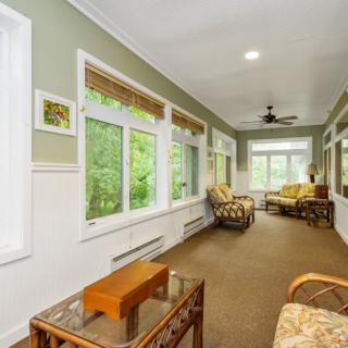 A bright sunroom with large windows, cozy furniture, and a view of the greenery outside.