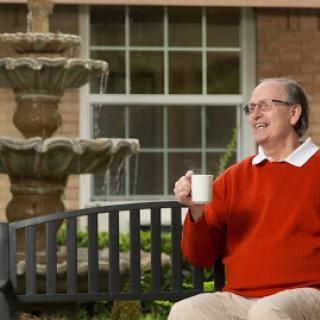 An elderly man enjoys a peaceful moment with a cup of coffee by the fountain.