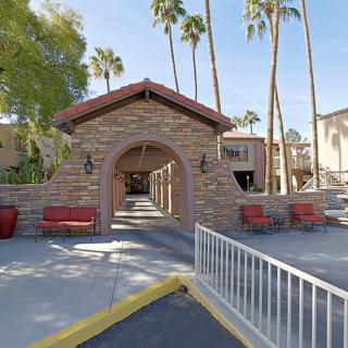 A stone archway leading to a walkway lined with palm trees on a sunny day.
