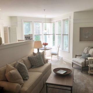 A cozy living room with natural light, featuring a sofa, armchair, and dining area.