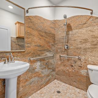 A modern bathroom featuring a shower with granite walls, a sink, and a toilet.