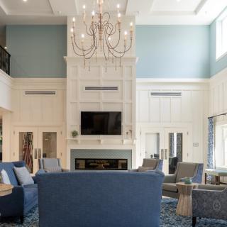 A spacious living room with a large chandelier, blue sofas, and a fireplace under a high ceiling.