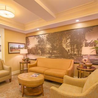 A warmly lit hotel lobby featuring comfortable seating, a central coffee table, and elegant artwork on the walls.