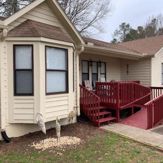 A residential house with a red porch and ramp, featuring multiple windows and a small yard.