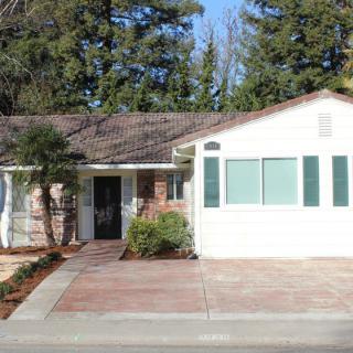 A single-story suburban house with a paved driveway and surrounding trees.