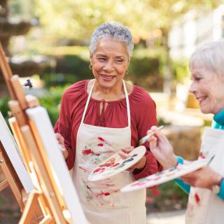 Two senior women enjoying painting together outdoors.