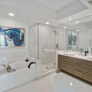 A modern bathroom featuring a glass shower, bathtub, and stylish vanity with contemporary art on the walls.
