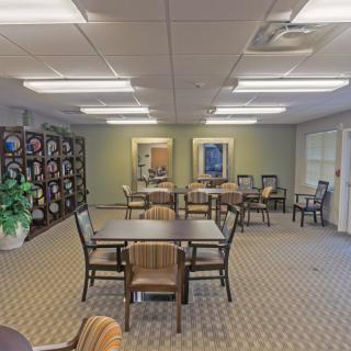 A well-lit dining area with multiple tables and chairs arranged neatly on a carpeted floor, featuring decorative elements and plants.
