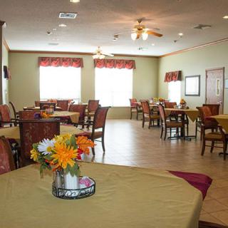 A well-lit dining area with neatly arranged tables and chairs, featuring floral centerpieces.