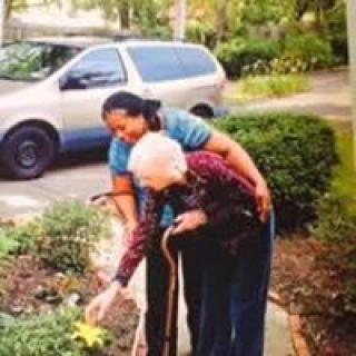 A caregiver assisting an elderly person in the garden.