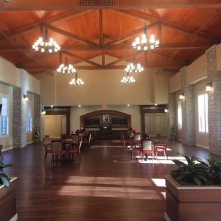 A spacious hall with wooden ceilings, chandeliers, tables, and chairs.