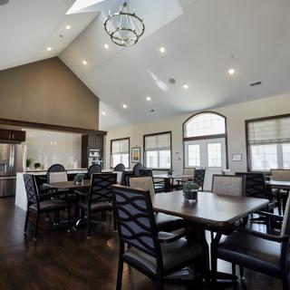 A modern dining room with multiple tables and chairs, featuring a kitchen area and contemporary lighting.