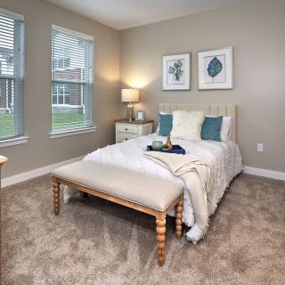 A cozy bedroom featuring a neatly made bed with decorative pillows, side tables with lamps, and framed artwork on the walls.