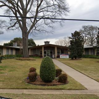 A mid-century modern building with a well-maintained lawn and landscaping under an overcast sky.