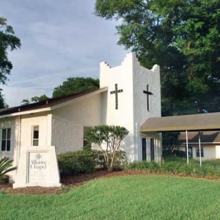 A small church building with crosses on the front, surrounded by greenery.