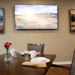 A cozy dining area featuring a neatly set table, wall art, and a television displaying a scenic view.