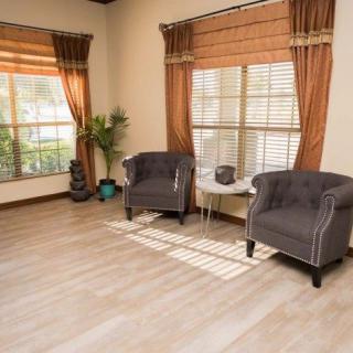 A cozy living room with two upholstered chairs and large windows, complemented by warm curtains and wooden flooring.