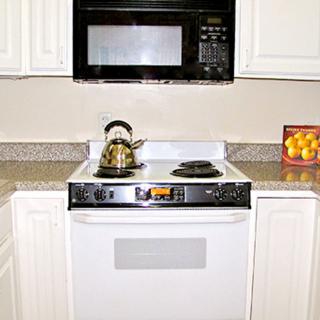 A kitchen stove with a teapot, beneath a microwave and next to a box of oranges on the countertop.