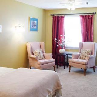 A cozy bedroom with two upholstered chairs and red curtains by the window.