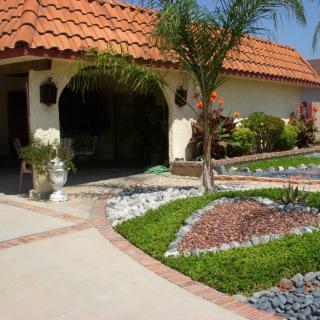A well-maintained garden with a palm tree and decorative rocks in front of a house with a tiled roof.