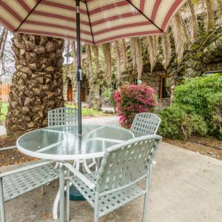 A cozy outdoor patio with a table, chairs, and an umbrella surrounded by lush greenery.