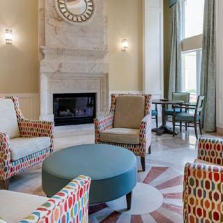 A stylish living room featuring patterned armchairs, a central ottoman, and a classic fireplace.