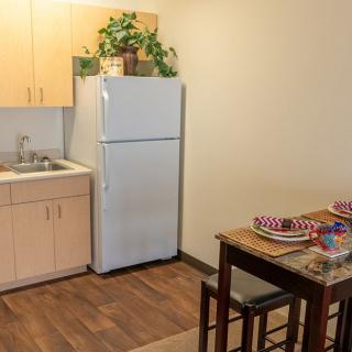 A compact kitchen and dining area featuring a refrigerator, sink, and a table with place settings.