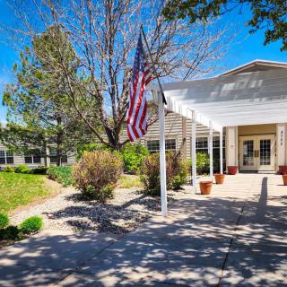 A building entrance with an American flag, surrounded by trees and landscaping on a sunny day.