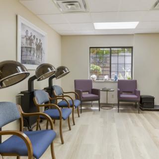 A well-lit salon waiting area featuring salon chairs with hair dryers and comfortable seating.