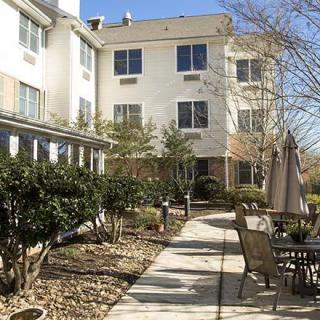 A sunny courtyard with a pathway, outdoor seating, and landscaped garden in front of a multi-story building.