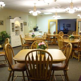 A cozy dining room with wooden tables and chairs, softly lit by overhead chandeliers.