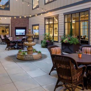 A cozy outdoor patio featuring a central fountain, surrounded by tables and chairs with string lights creating an inviting ambiance.