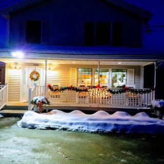 A cozy house with a decorated porch and snow-covered ground at night.