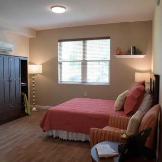 A cozy bedroom with subtle lighting, featuring a neatly made bed, classic furniture, and decorative elements.