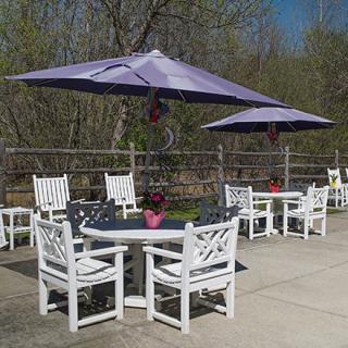 An outdoor patio area with white tables and chairs, shaded by purple umbrellas.